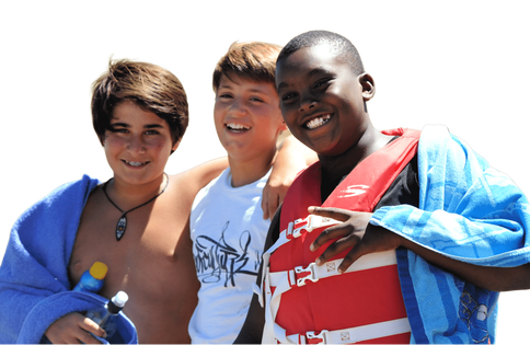 Three teenage boys holding sunscreen and towels enjoying the beach at summer camp in Hawaii.