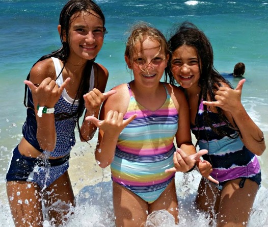 Three girls giving in the ocean giving hang loose sign at Aloha Beach Camp's Aloha Hawaii Sleepaway Summer Camp 2024